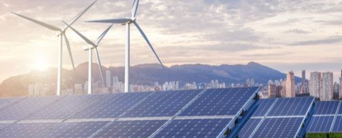 Sun setting across landscape of solar panels, green grass, and wind turbines