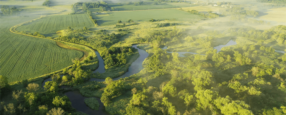 An aerial view of green fields with trees lining a small creek.